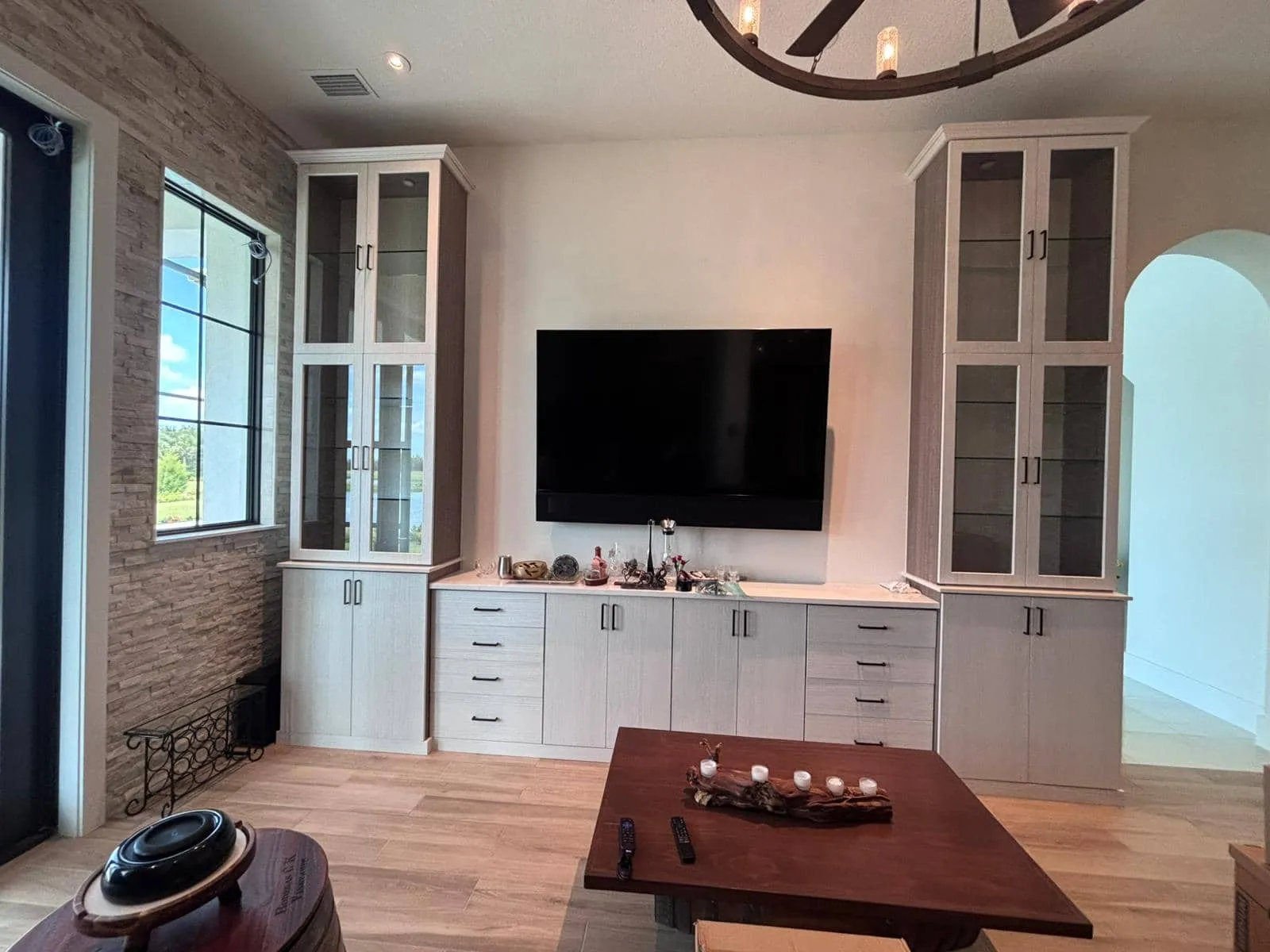 Custom media center with glass-front display towers against a stacked-stone accent wall in Sarasota, FL