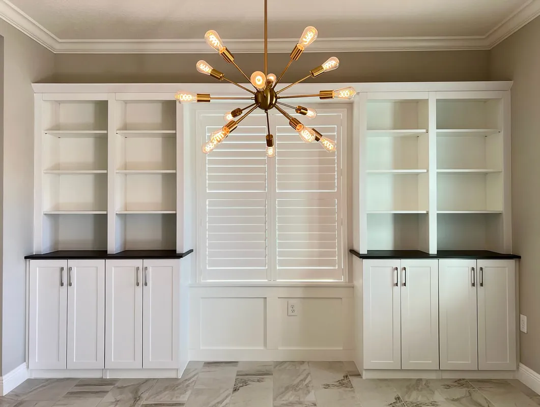 Twin custom built-in bookcases with black stone countertops flanking a shuttered window